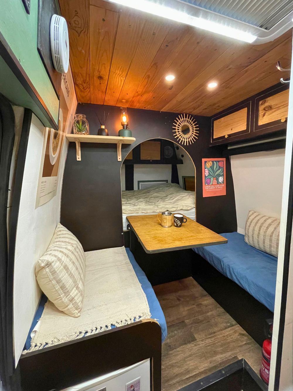 Intérieur d'un van aménagé par Roues Libres : couchage, table, banquettes et rangements en bois